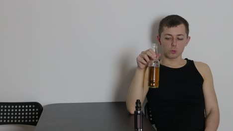 joven caucásico deprimido sentado solo dentro de una habitación vaping y bebiendo cerveza
