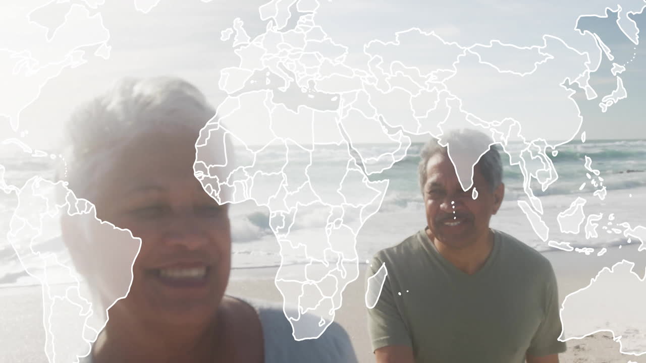 Senior couple walking together on sandy beach, showcasing global map overlay for business growth