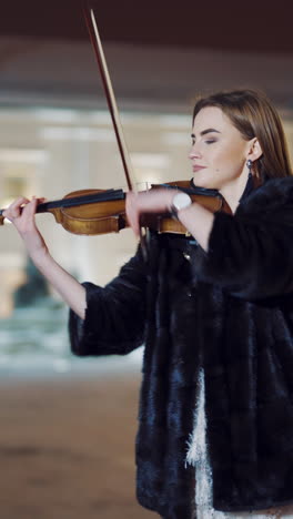 a talented girl performs composition on the instrument on the background of tall buildings in the city center. the musician plays the violin in the evening. blurred background. vertical video