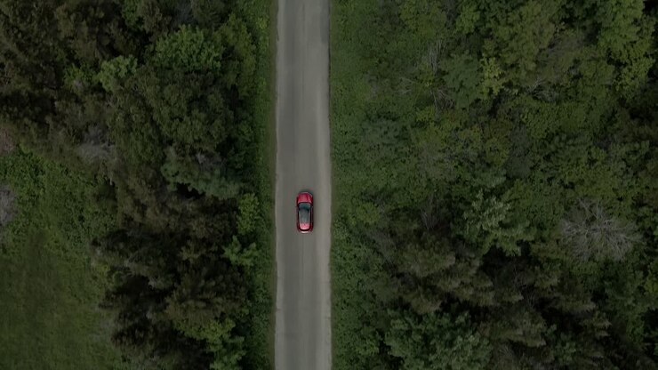 Veduta dall'alto di un'auto di lusso a marchio Infiniti rossa che guida su una strada rurale con alberi rigogliosi in Canada - drone aereo