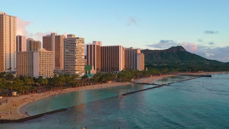 crowded beach with people swimming inside breakwall and diamond head tuff cone overlooking kuhio beach in waikiki, hawaii