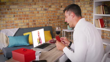 Caucasian-couple-making-valentines-date-video-call-woman-holding-flowers-on-laptop-screen