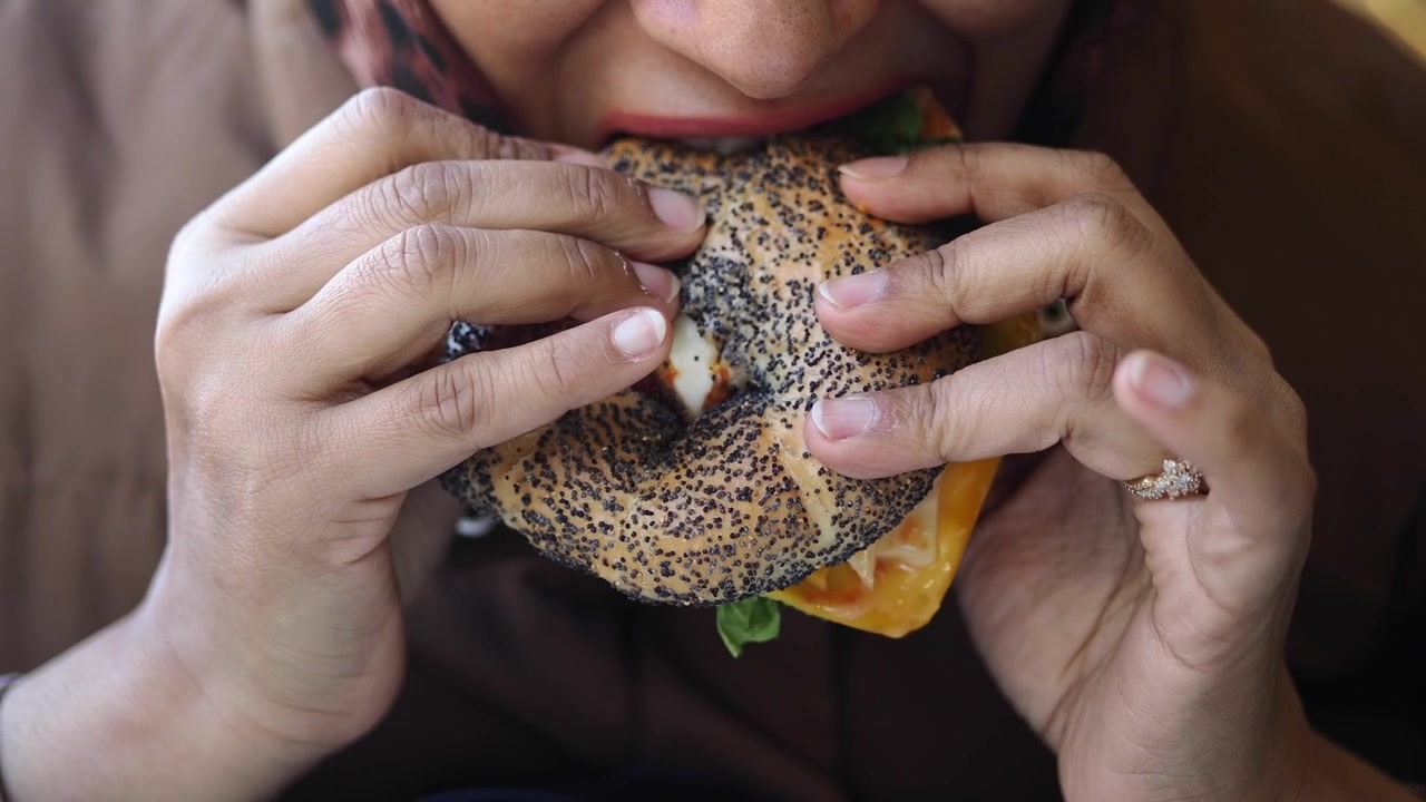 Person Eating a Poppy Seed Bagel Sandwich