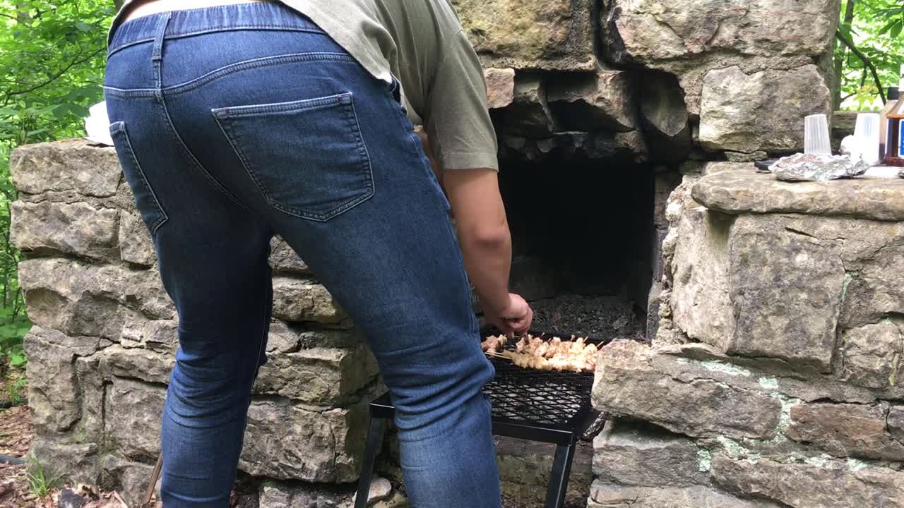 hombre en jeans asando barbacoa en horno hecho con ladrillos en la naturaleza