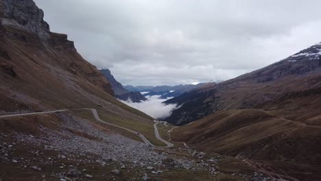 Drone-shot-of-rocky-mountain-landscape-criss-crossed-by-winding-road-and-foggy-valley-in-the-background