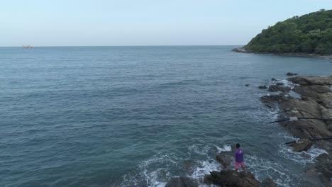 Flying-over-a-man-fishing-in-the-ocean-from-rocks