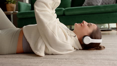 listening to music with headphones, woman lying on floor and smiling, at home