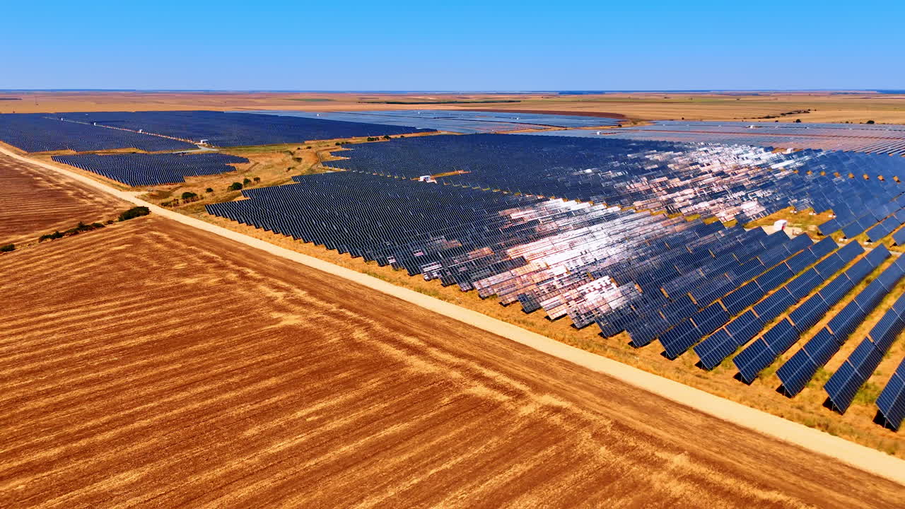 Aerial photo of solar panels in wide field. Solar power plant with hundreds of panels built in dry yellow fields under blue sky