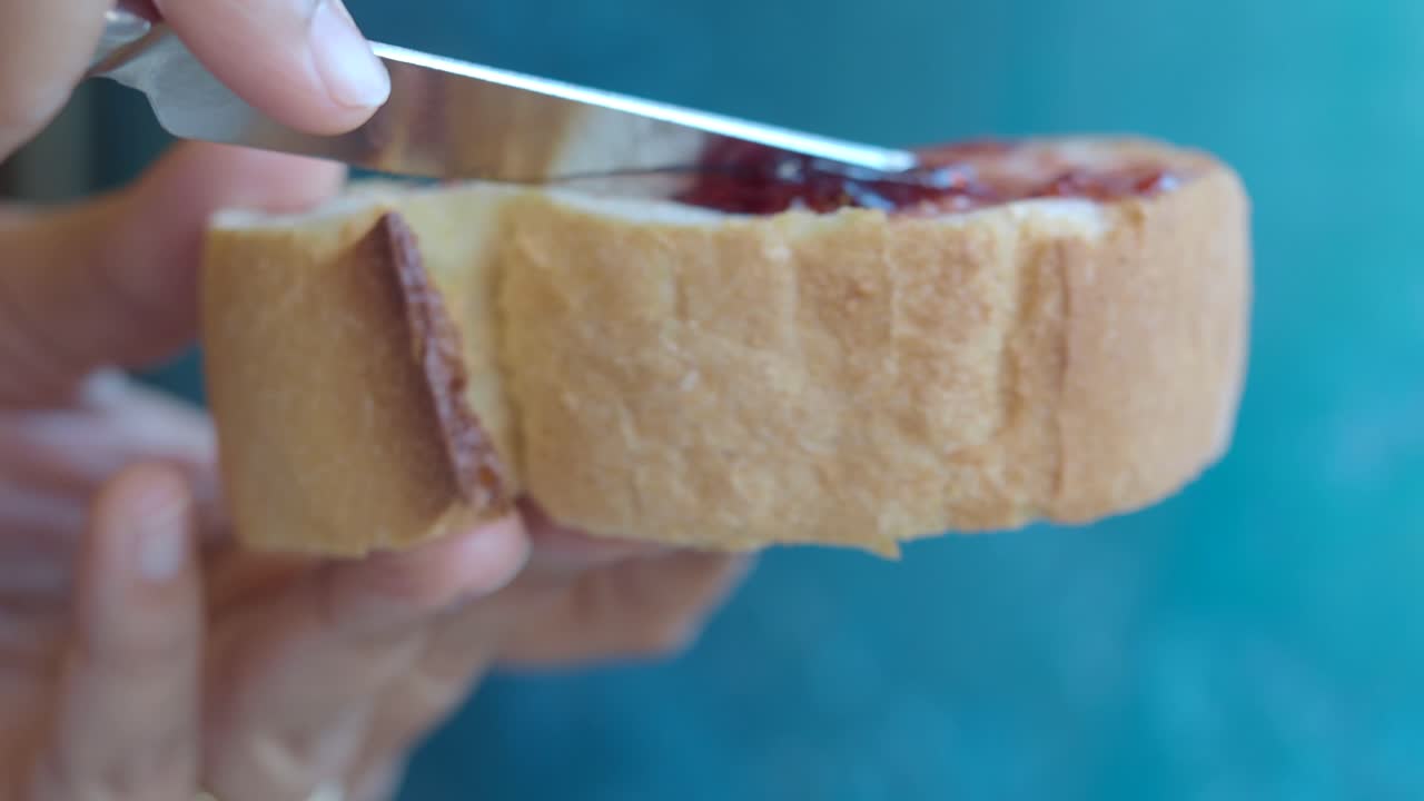 Hand cutting a slice of bread with jam