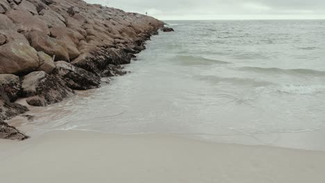 soft waves meet rocky shoreline and sand under cloudy sky