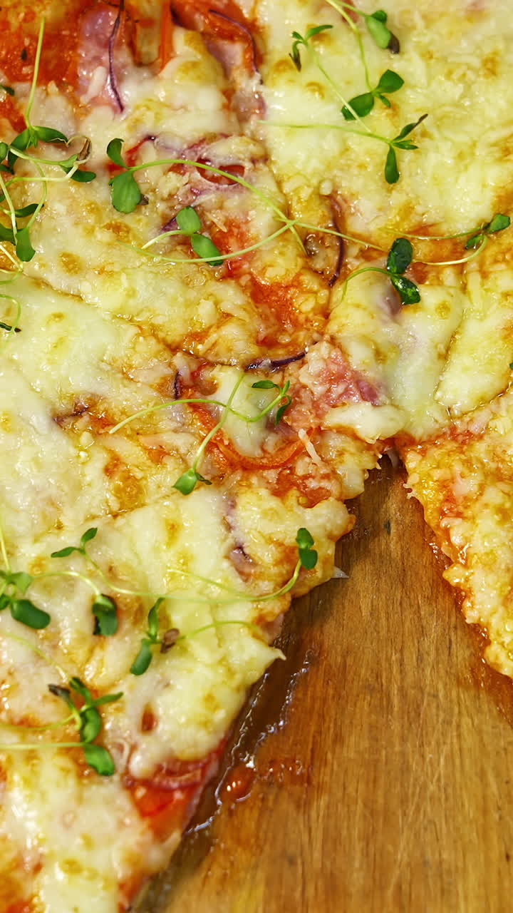 Fresh pizza spinning on the table. Delicious pastry with melted cheese, tomatoes and meat in pizzeria. Well baked pizza without one portion on table. Vertical video