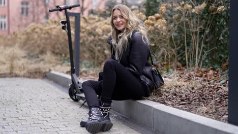 stylish woman sitting beside electric scooter in city park