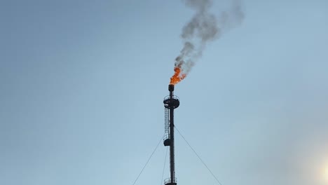 close-up telephoto of gas flare burning against clear blue sky, zoom out