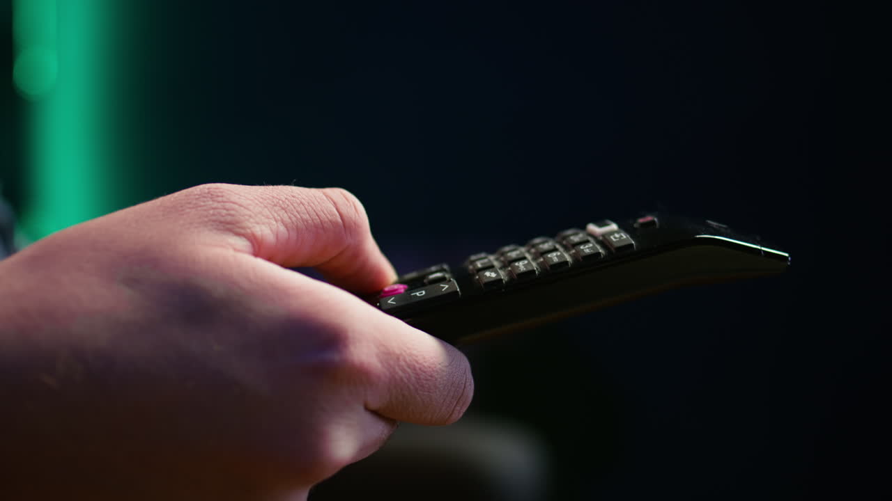 tv의 채널을 가로질러 리모컨을 사용하여 소파에 있는 남자의 클로즈업