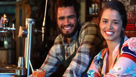 portrait of smiling barmaid and barman with cocktail shaker and cocktail at bar counter