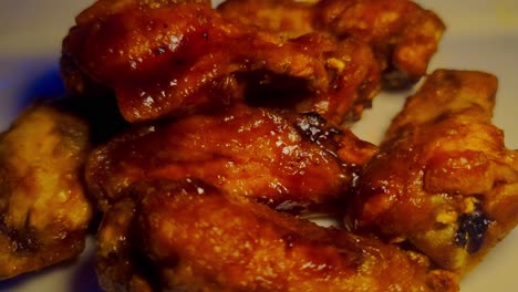 bbq chicken wings on a plate piled up saucy drums zoom in closeup white ceramic plate in a pub with yellow lights