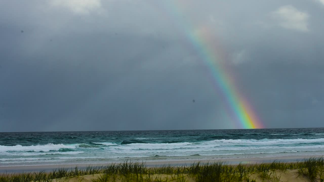 tormenta sobre el pacífico: un arco iris vívido y dramático atraviesa el cielo de la tormentosa y amenazante escena oceánica.