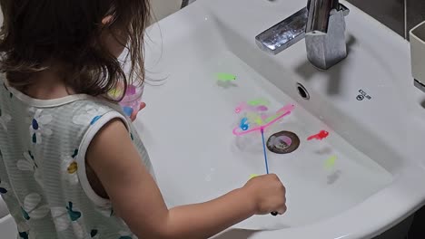la parte trasera de una niña de tres años jugando al juego de pesca en el fregadero del baño