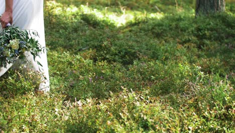 low shot of a just marriend couple walking in the forest with the wife holding a bouquet