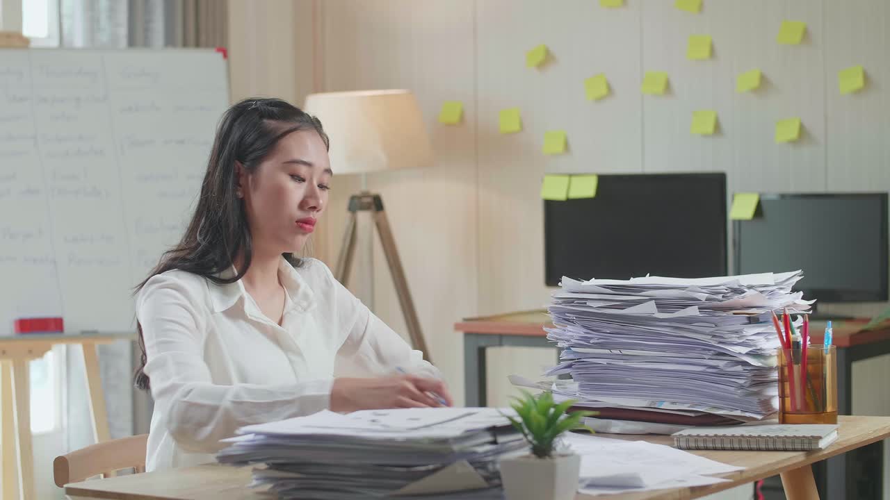 Asian Woman Writing Something On Paper While Working With Documents At The Office