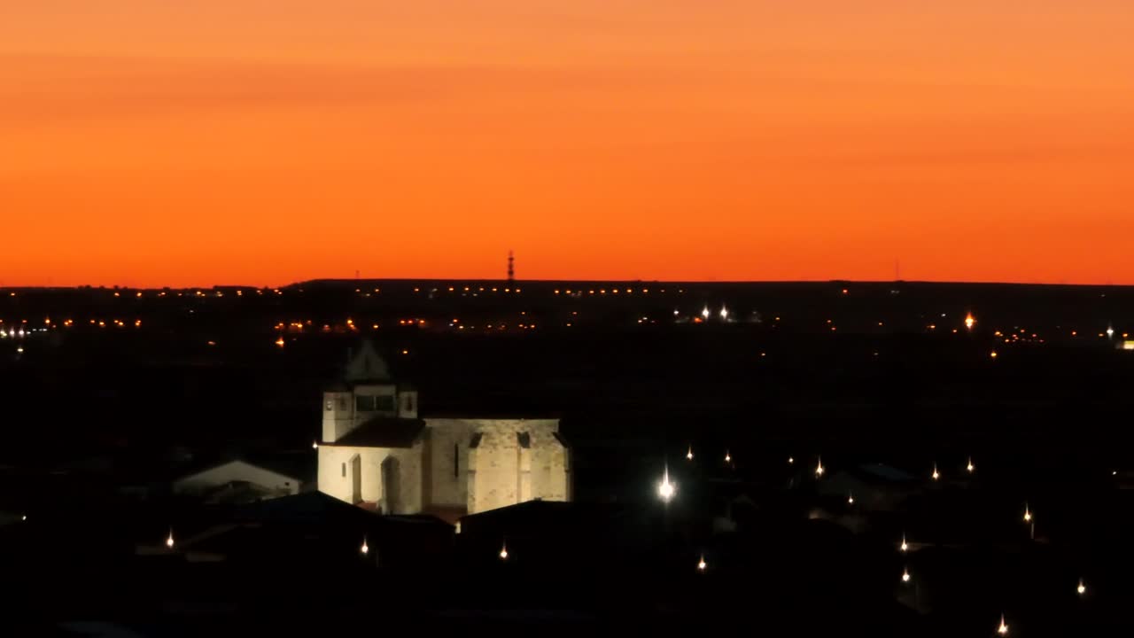 묵시적인 오렌지색 일몰 하늘을 배경으로 교회 건물을 둘러싼 공중 스포트라이트