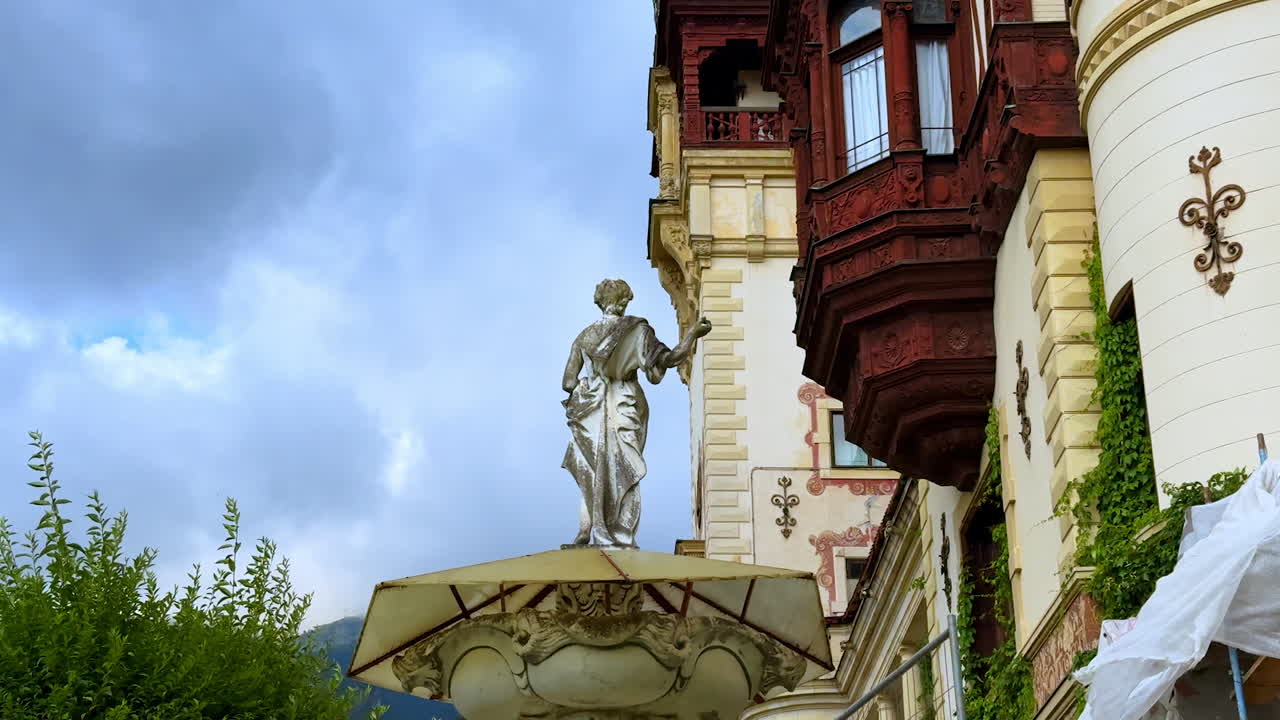 Female statue outdoors near the old style buildings. Low angle view at the façade of the Peles Castle in Prahova County, Romania and cloudy sky