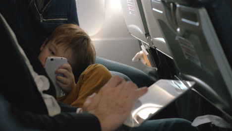 child with cell and and man using pad in plane