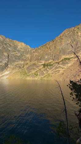 Vertical-View,-Hiker-bt-Pristine-Glacial-Lake,-Some-Ice-and-Sunny-Rocky-Mountain-Hills,-Panorama