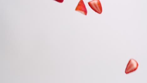 bright red strawberry half pieces raining down on white backdrop in slow motion