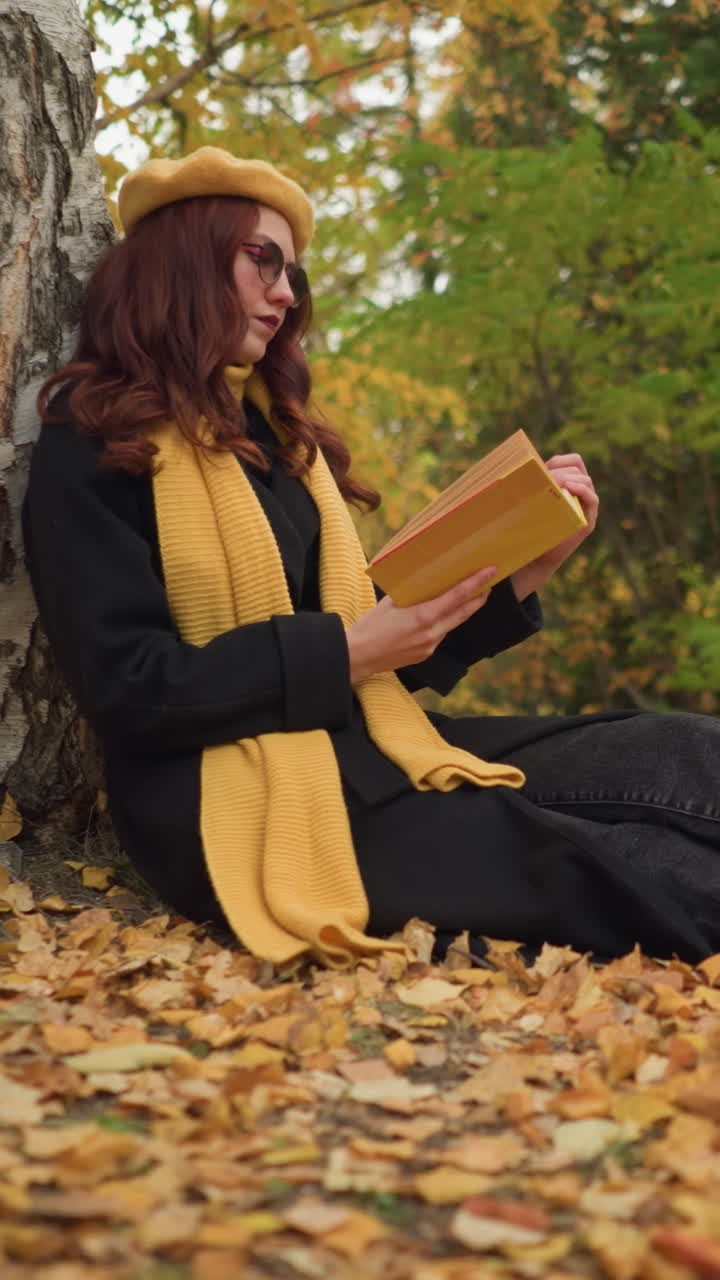 una elegante dama con boina amarilla se sienta al aire libre, con las piernas cruzadas, apoyada en un árbol, leyendo un libro en medio de las hojas de otoño caídas, disfrutando de la tranquila soledad, rodeada de la belleza de la naturaleza