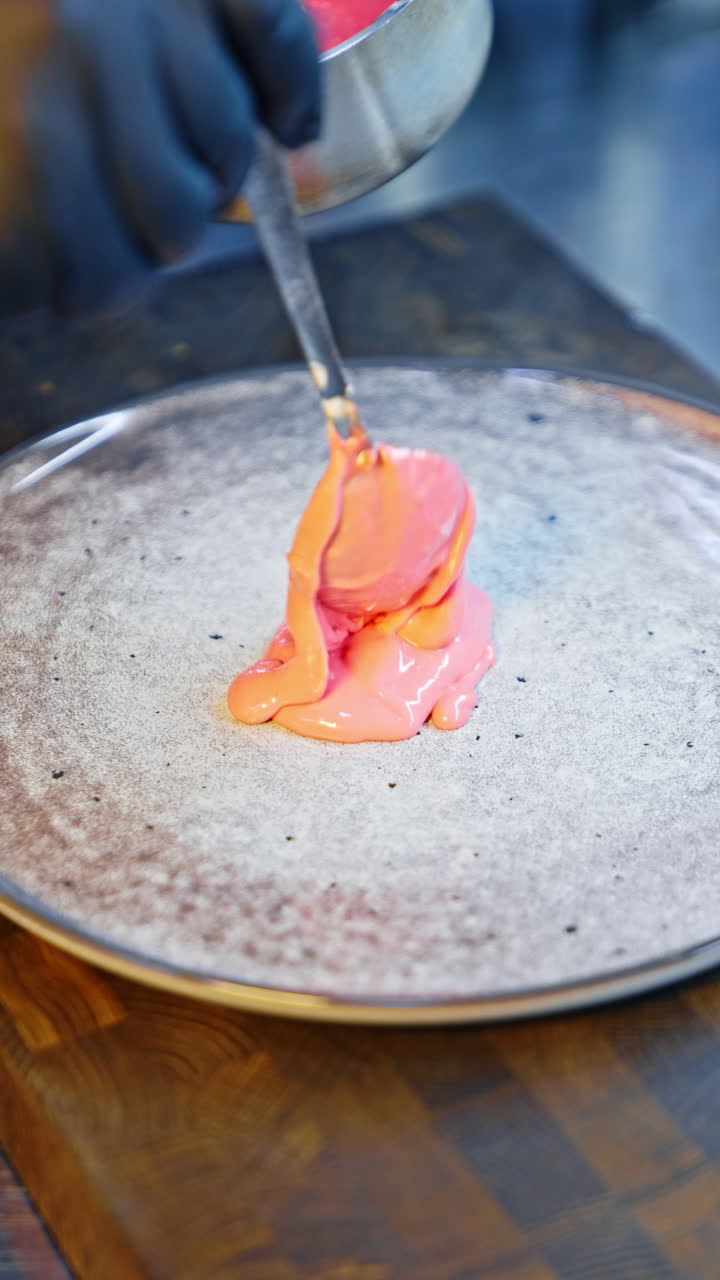Cook puts some pink sauce from the pan onto the plate using a spoon. Chef spreads the sauce by the plate. Close up. Vertical video.