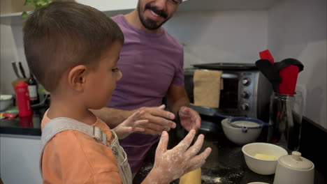 mexican latin father cleaning his son's nose covered in flour while they prepare a cake in the kitchen having fun