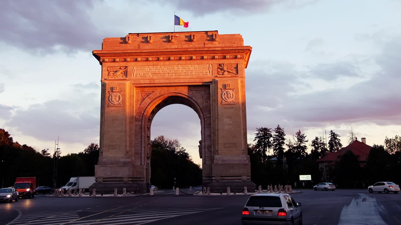 Bucharest, Romania - April 24, 2021: Cars moving near The Triumphal Arch at sunset