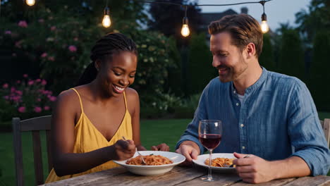 couple enjoying a romantic outdoor pasta dinner under string lights