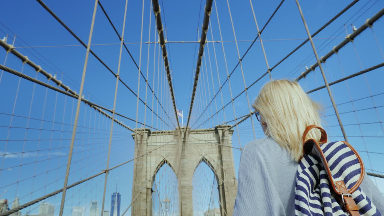 미국 국기를 든 관광객과 백패커가 뉴욕의 유명한 브루클린 다리를 따라 걷고 있다