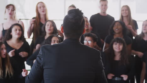 estudiantes masculinos y femeninos cantando en el coro con el maestro en la escuela de artes escénicas