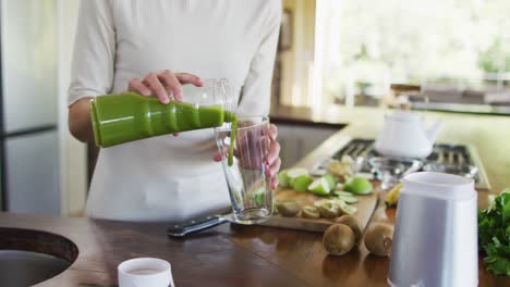 midsection of biracial woman pouring smoothie to glass in kitchen