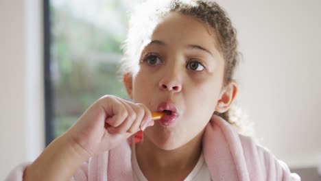 feliz chica de raza mixta cepillándose los dientes en el baño