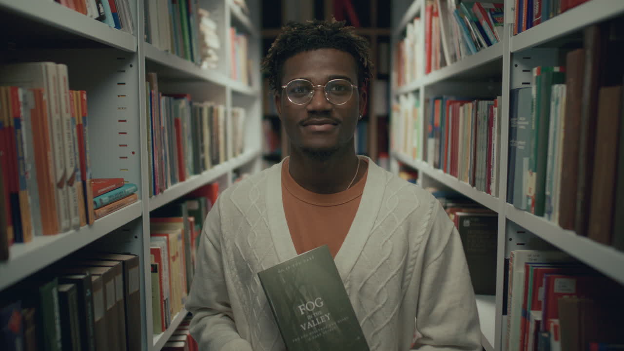 retrato de un joven negro sosteniendo un libro en el pasillo de la biblioteca
