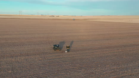 Farmer-with-quad-taking-earth-sample-in-farm-field,-aerial-reveal