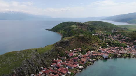 vista de avión no tripulado en albania volando sobre una pequeña ciudad con casas al lado de una colina verde en el lago ohrid con agua azul cristalino