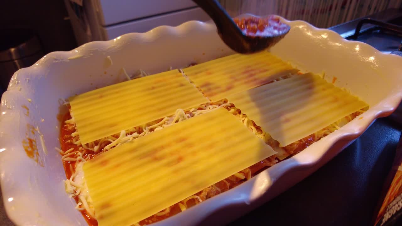 숟가락으로 라자냐 파스타 시트 위에 뜨거운 김이 나는 볼로네제 소스를 붓고 있습니다.