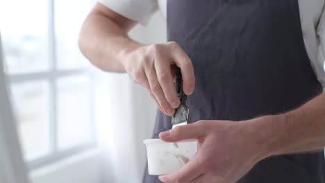 the artist stands and stirs the white paint in the vessel with a spatula - the artist stands and stirs the white paint in the vessel with a spatula. creative workshop in white tones. the process of creating a picture. brush movement