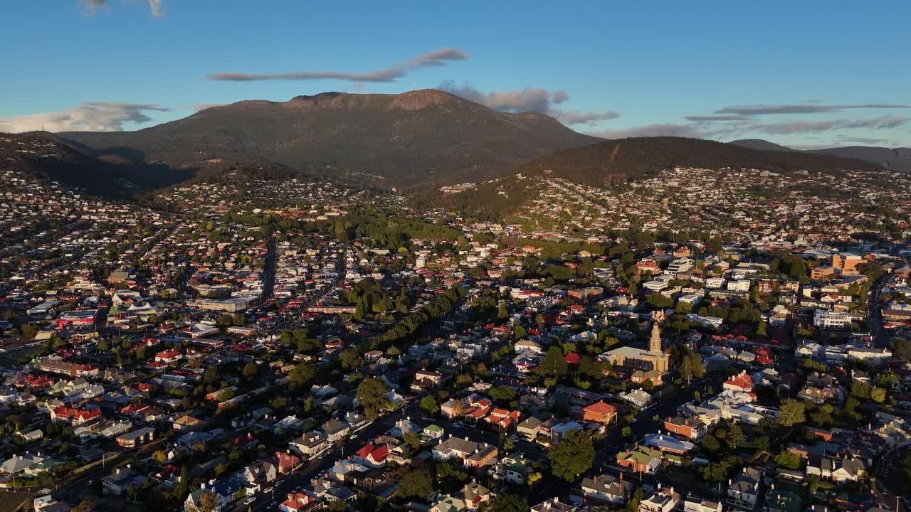 Tasmanian cityscape with Mount Wellington in background. Sunset time over Hobart Town, Tasmania. Neighborhood with houses and homes in summer. Aerial flyover wide shot.