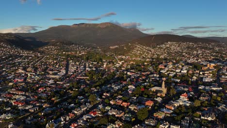 tasmanian cityscape with mount wellington in background. sunset time over hobart town, tasmania. neighborhood with houses and homes in summer. aerial flyover wide shot.