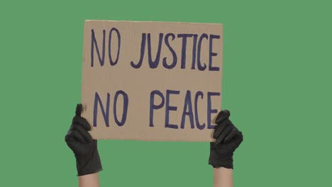 female hands in black gloves pick up a poster from a cardboard box that reads no justice no peace. cardboard banner. isolated a green screen, chroma key. close up. slow motion