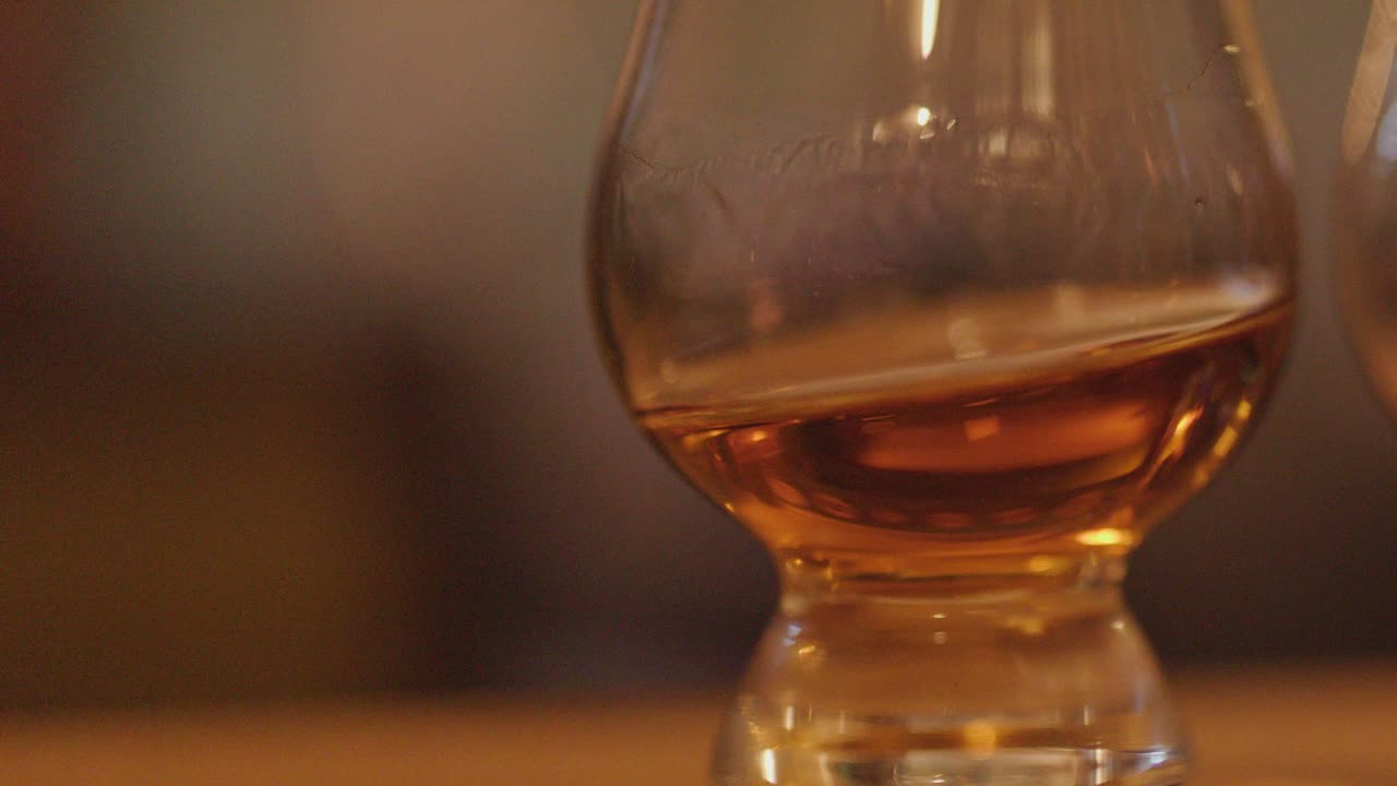 Amber whiskey swirling in a tasting glass on a wooden bar with warm, soft lighting