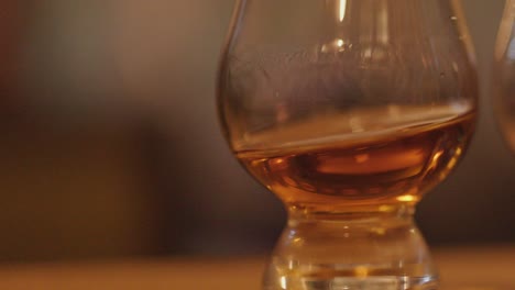 amber whiskey swirling in a tasting glass on a wooden bar with warm, soft lighting