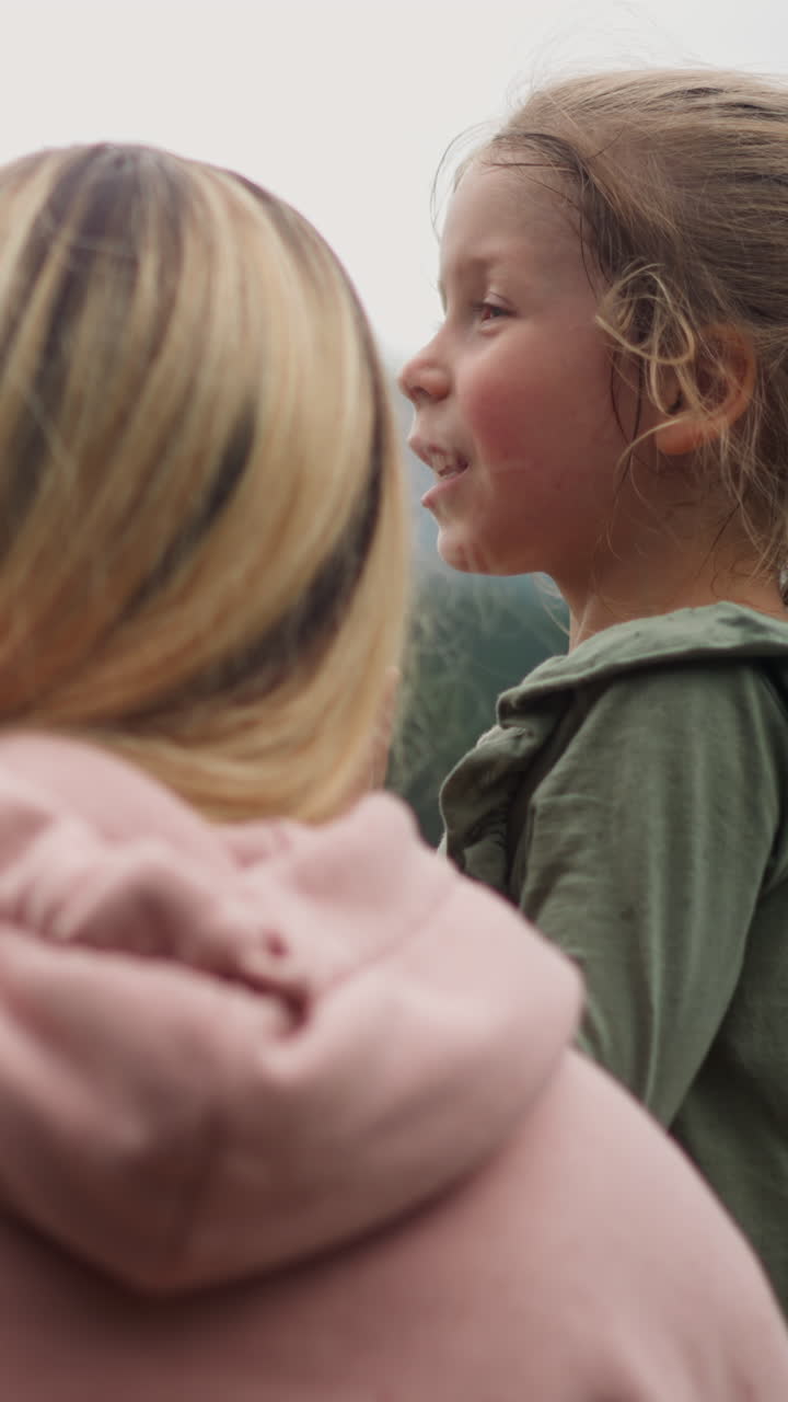 Happy woman and little son with playful daughter look at distant mountains covered with deep forest on gloomy spring rainy day backside view
