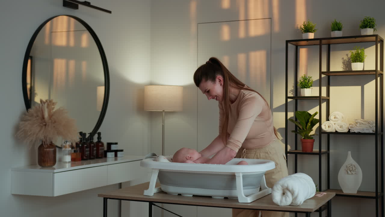 Mor bader forsiktig nyfødt baby i bærbart badekar i et moderne baderomsmiljø som fremmer hygiene